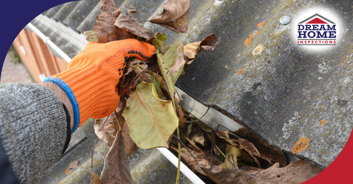 Hand in orange gloves removing leaves from a roof gutter.