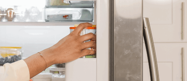 Smiling woman placing food into a refrigerator in a modern kitchen.