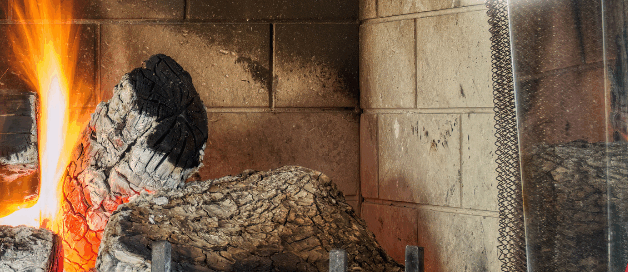 Burning logs in a brick fireplace with glowing embers and flames.
