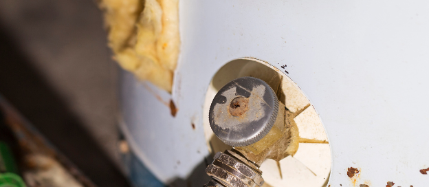 Close-up of a rusted water heater with a hose attached.